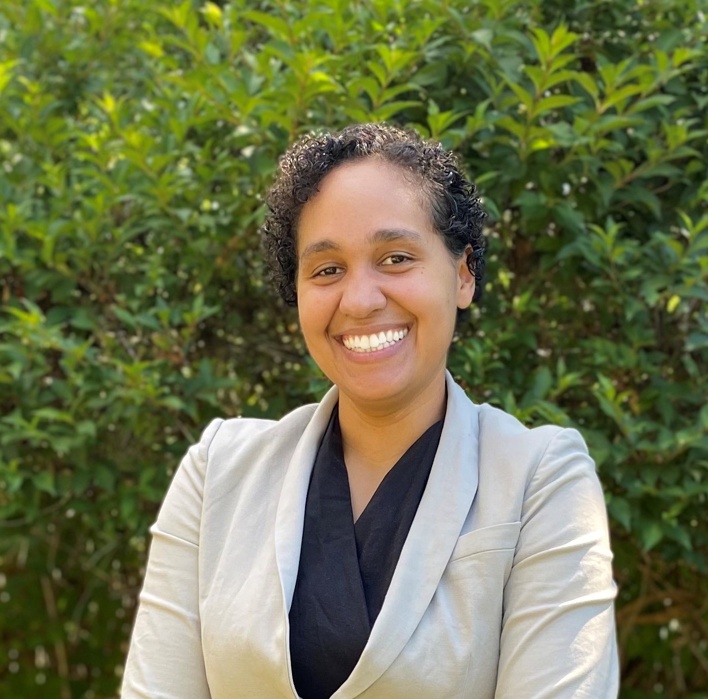 Teresa Hepler in a black shirt and tan blazer in front of green foliage